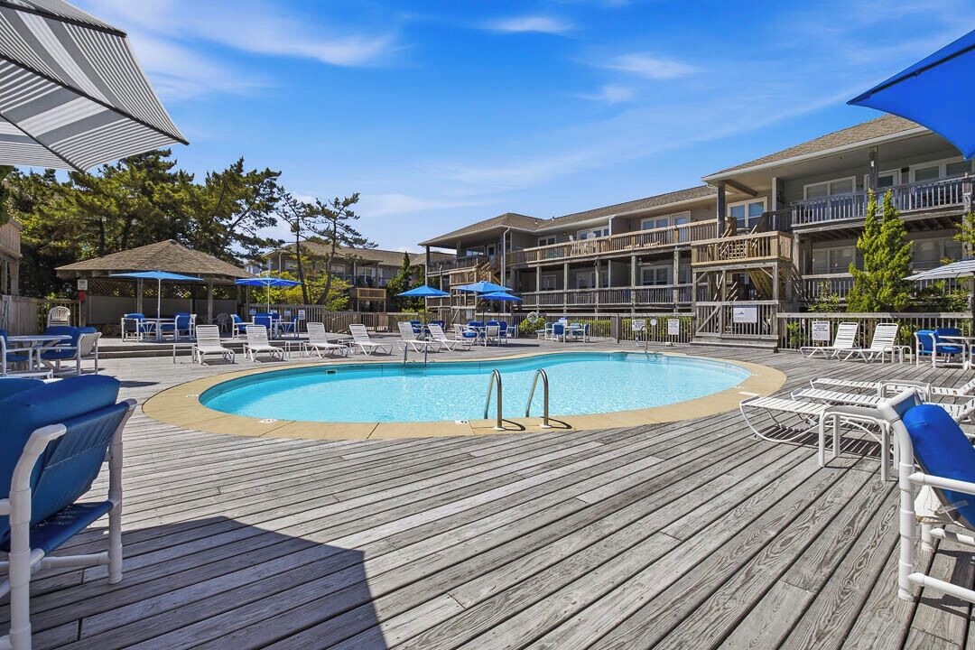 A pool area with lounge chairs and umbrellas, surrounded by multi-story buildings with balconies.