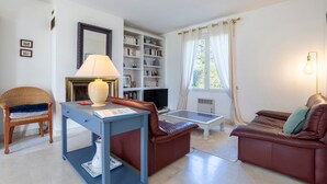 A living room with a sofa, a table, a chair, a bookshelf, and a television. - Ty Mamm – 5 min from Beach – 3 Bedrooms – Sleeps 6 (Guilvinec)