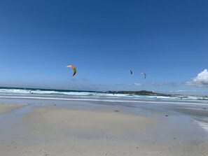 Una playa con cielo despejado y tres cometas volando.