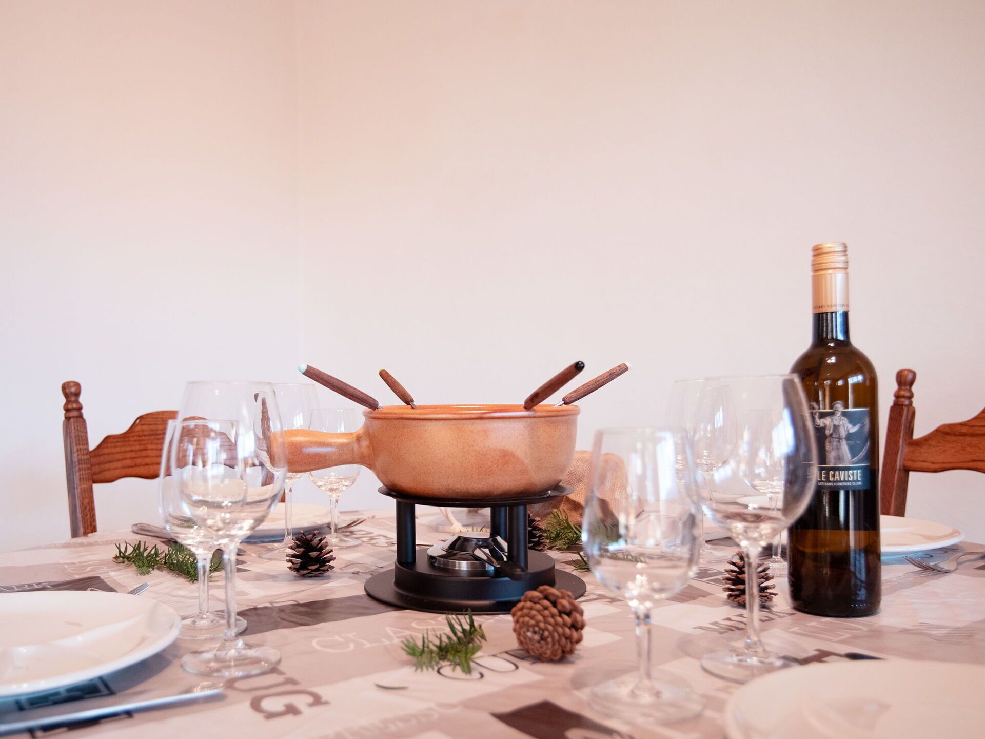 Une table à manger dressée avec des assiettes, des verres, une bouteille de vin et un réchaud portable.
