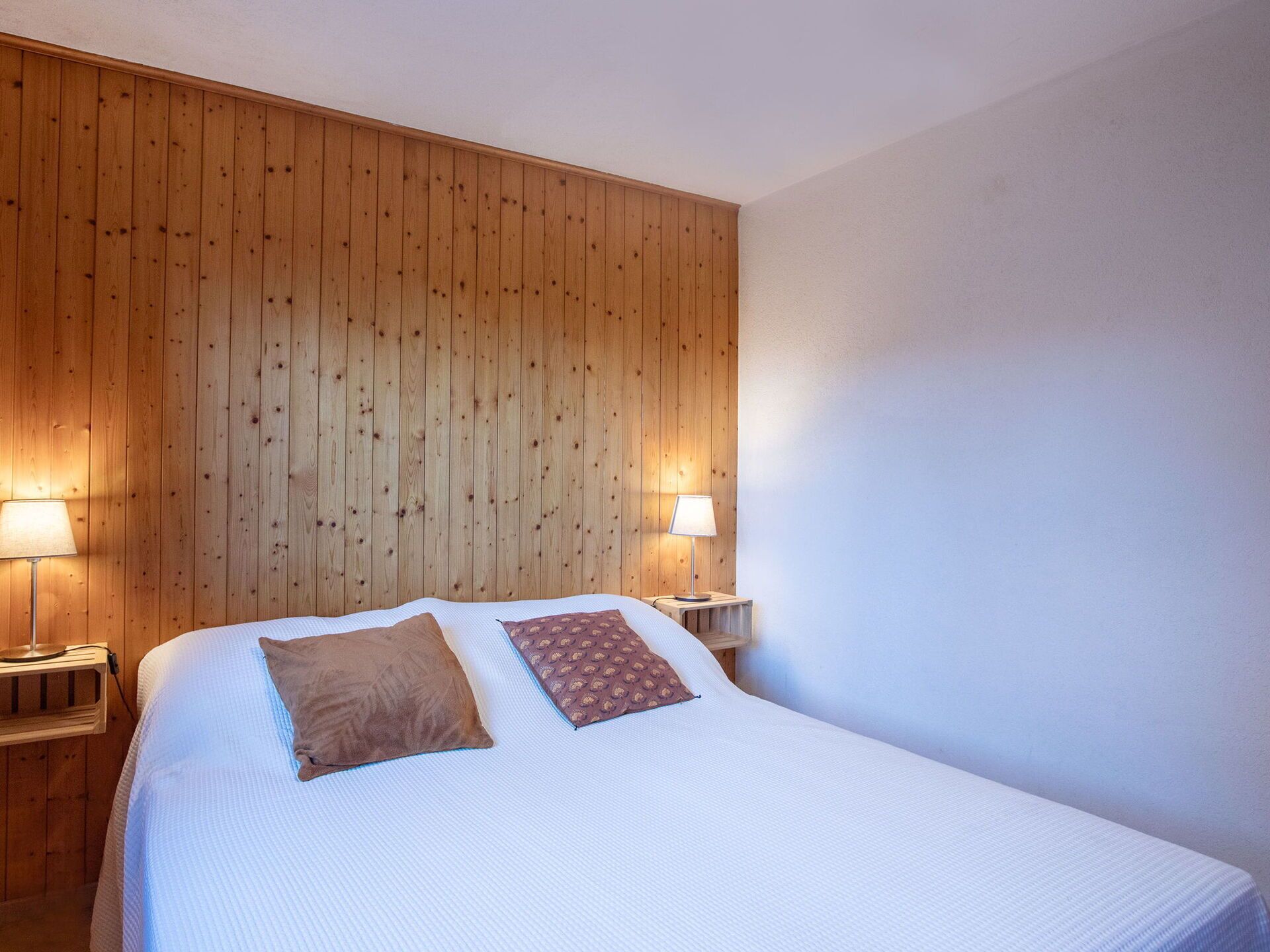 A hotel room with a wooden panel wall, a large bed with two pillows, and two bedside lamps.