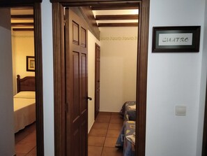 Un couloir étroit mène à une porte qui donne sur une chambre. On aperçoit un lit dans la pièce, et un panneau encadré accroché au mur porte l’inscription « CUATRO ».