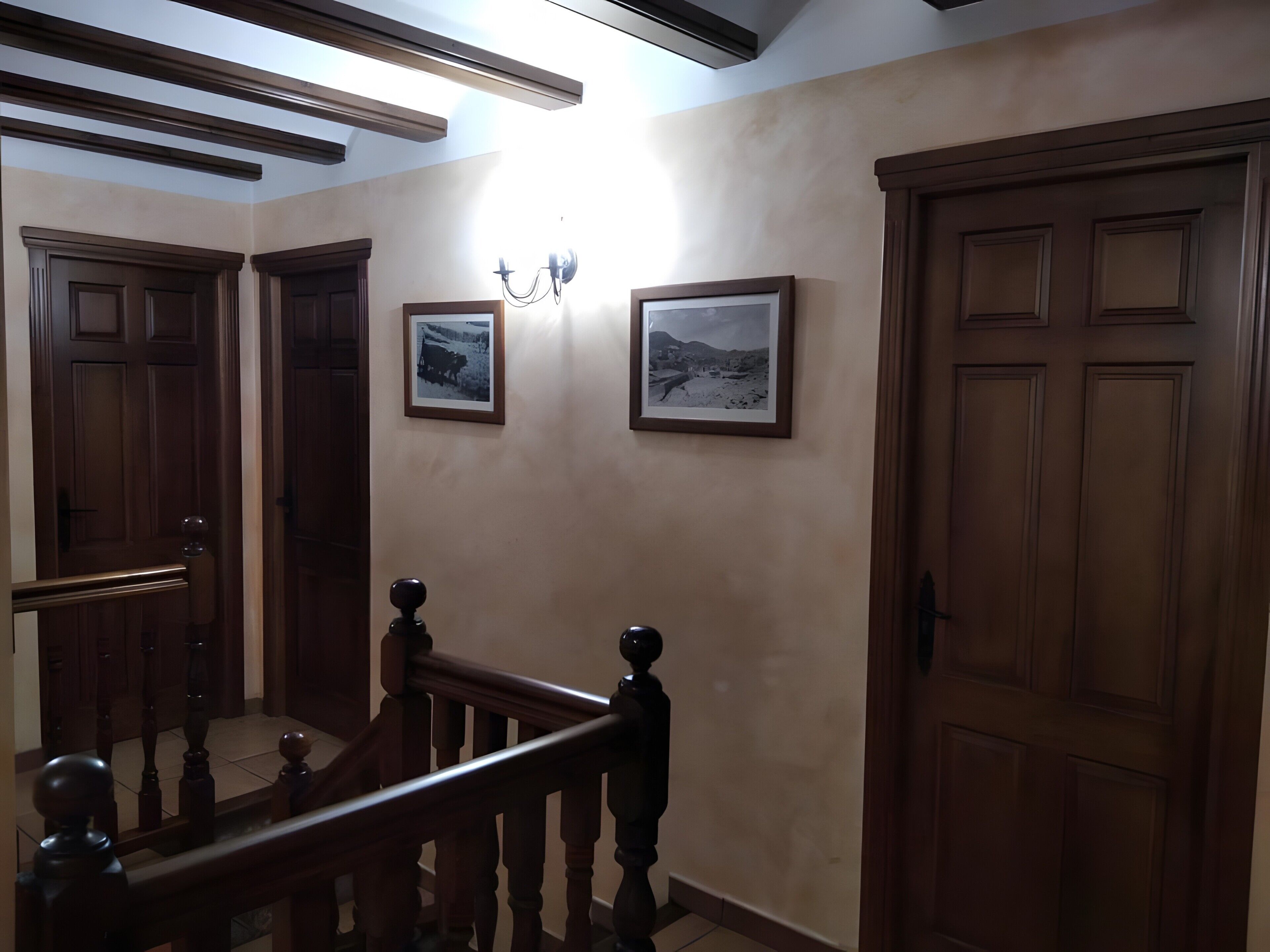 Um corredor com portas de madeira, uma escada com corrimão de madeira e duas molduras com imagens na parede.
