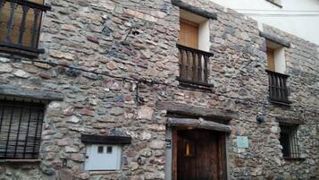 Un edificio de piedra con puerta de madera, una ventana pequeña con persiana y un balcón con barandilla de metal.