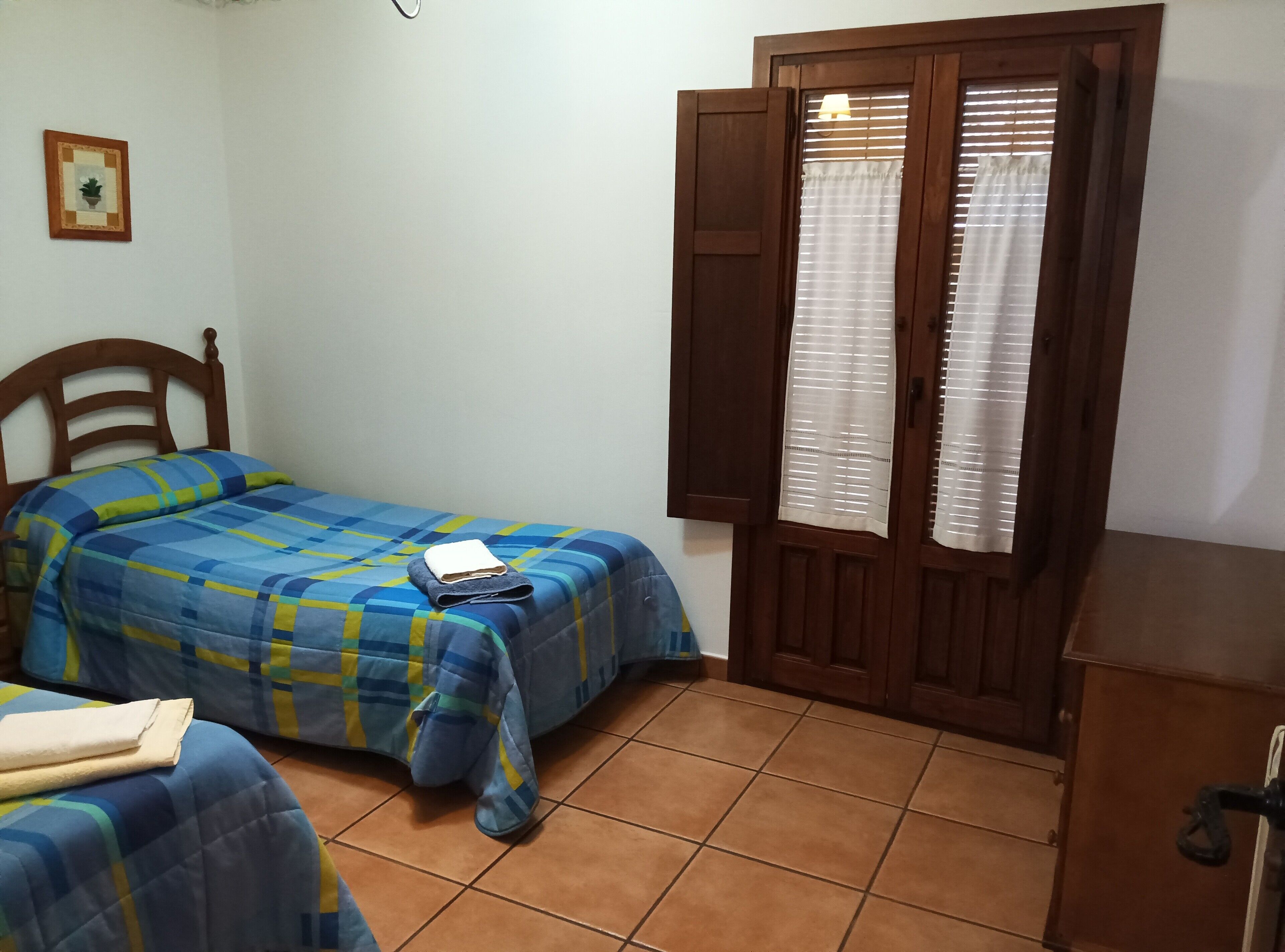 A bedroom with a bed, a wooden wardrobe, a window with curtains, and a small wall-mounted picture.