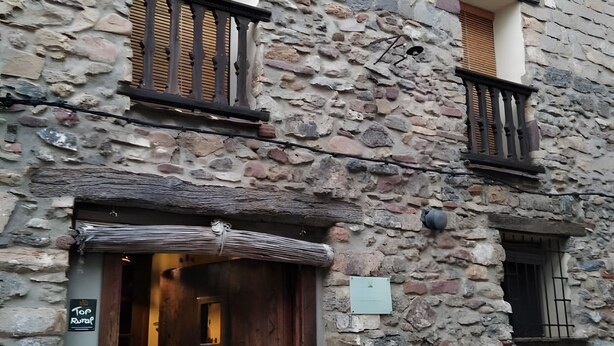 A stone building with a wooden door, a balcony, and a small window.