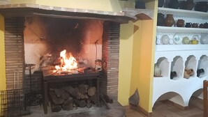 A fireplace with a fire, a brick wall, and a shelf with pottery.