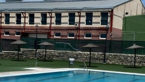 A swimming pool with a stone wall and umbrellas, a building with multiple windows in the background.