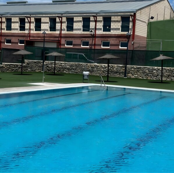 Une piscine avec un mur en pierre et des parasols, et un bâtiment avec de nombreuses fenêtres en arrière-plan.