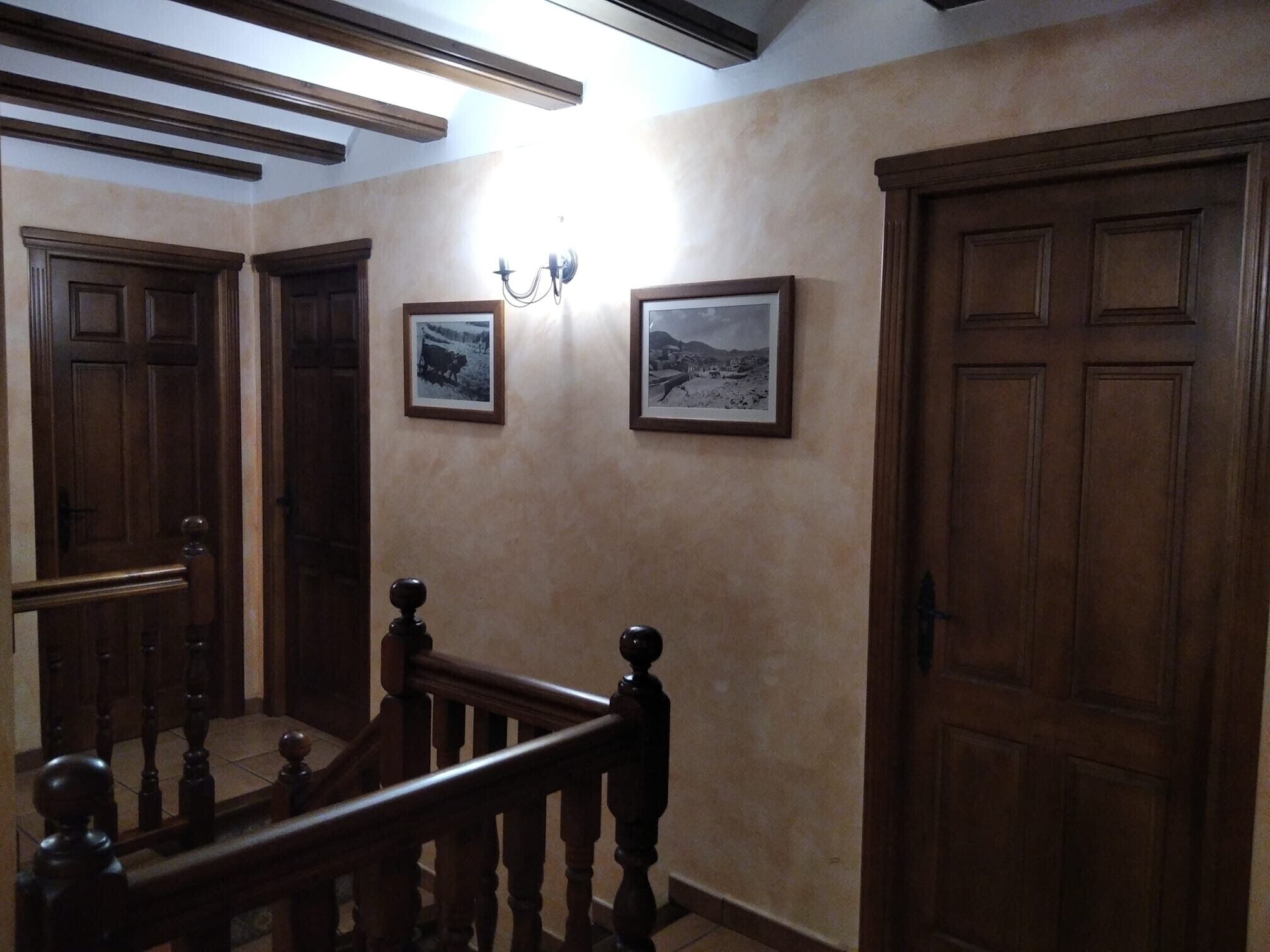 Un couloir avec des portes en bois, un escalier et deux tableaux encadrés accrochés au mur.