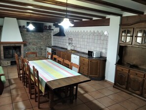 Una cocina con mesa de comedor, sillas, pared de piedra, microondas y armarios de madera.