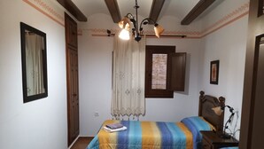 A bedroom with two beds, a wooden wardrobe, a ceiling light fixture, a window with blinds, and a framed picture on the wall. - Country House 'La Cisterna II' (Pina de Montalgrao)