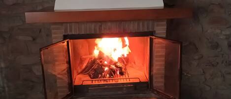 A fireplace with a stone wall, a wooden mantel, and a basket of logs.