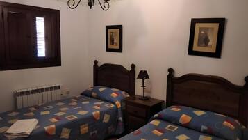 Un dormitorio con dos camas, un radiador, una lámpara fijada a la pared y cuadros enmarcados.