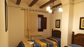 Camera da letto con due letti, un termosifone, una finestra con persiane, un lampadario e un quadro appeso al muro.