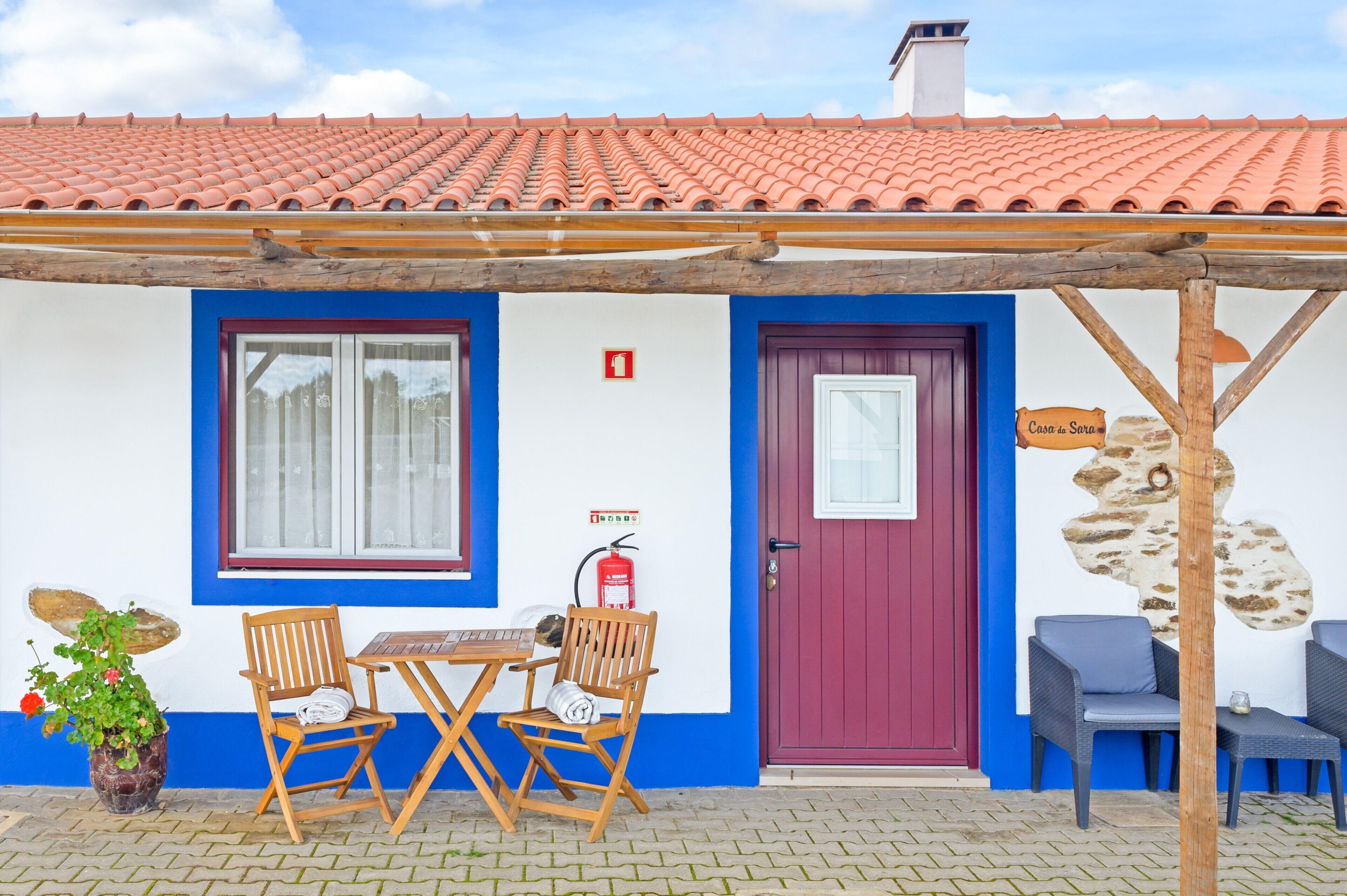 Un bâtiment avec un toit recouvert de tuiles rouges, une façade bleue et blanche, une pergola en bois et une enseigne indiquant « Casa da Sara ».