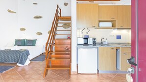 Un dormitorio con una escalera de madera, una cama con almohadas verdes y una cocina con armarios de madera y un microondas.