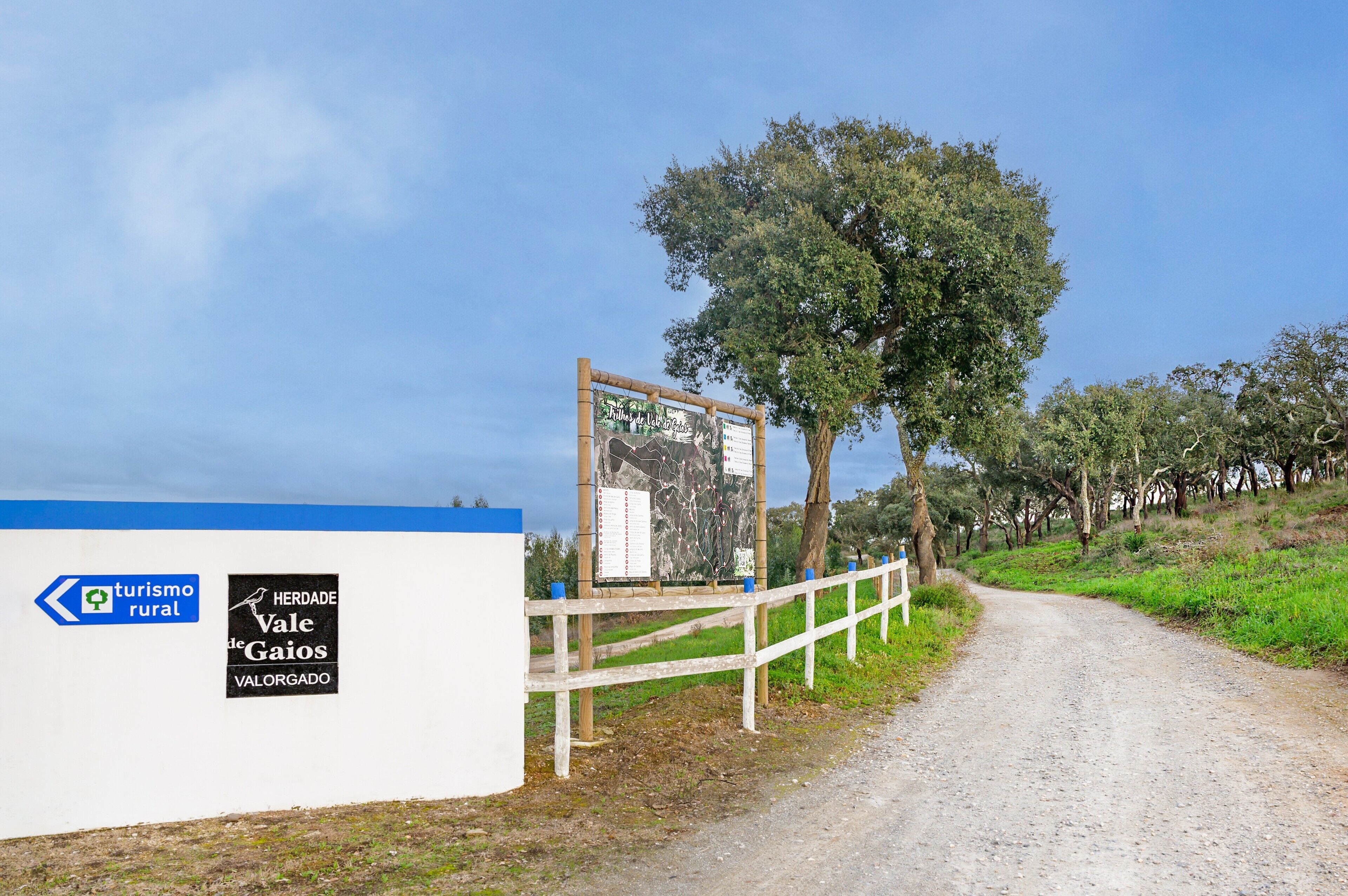 A rural road with a signboard and a white fence.