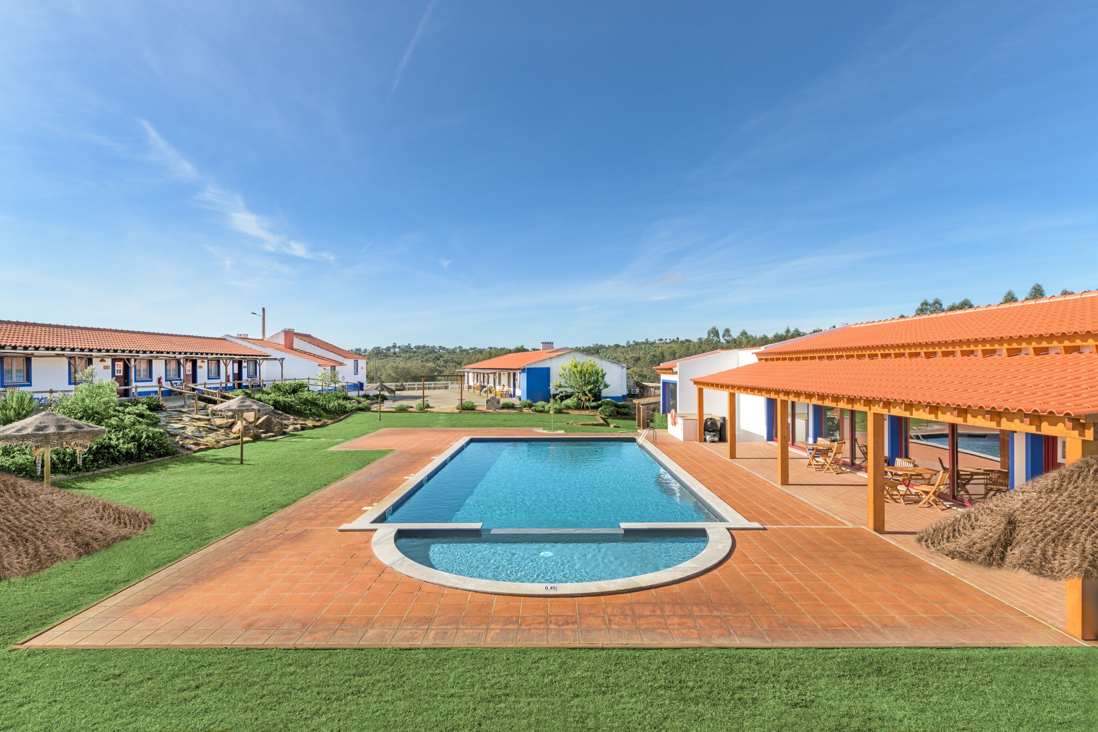A swimming pool with a surrounding deck, adjacent buildings, and a clear sky.