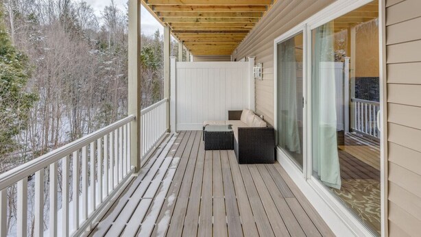 A covered deck with a sofa and table, large sliding glass doors, and a view of trees. - Luxe Condo-Shuttle & Amenities (Lincoln)