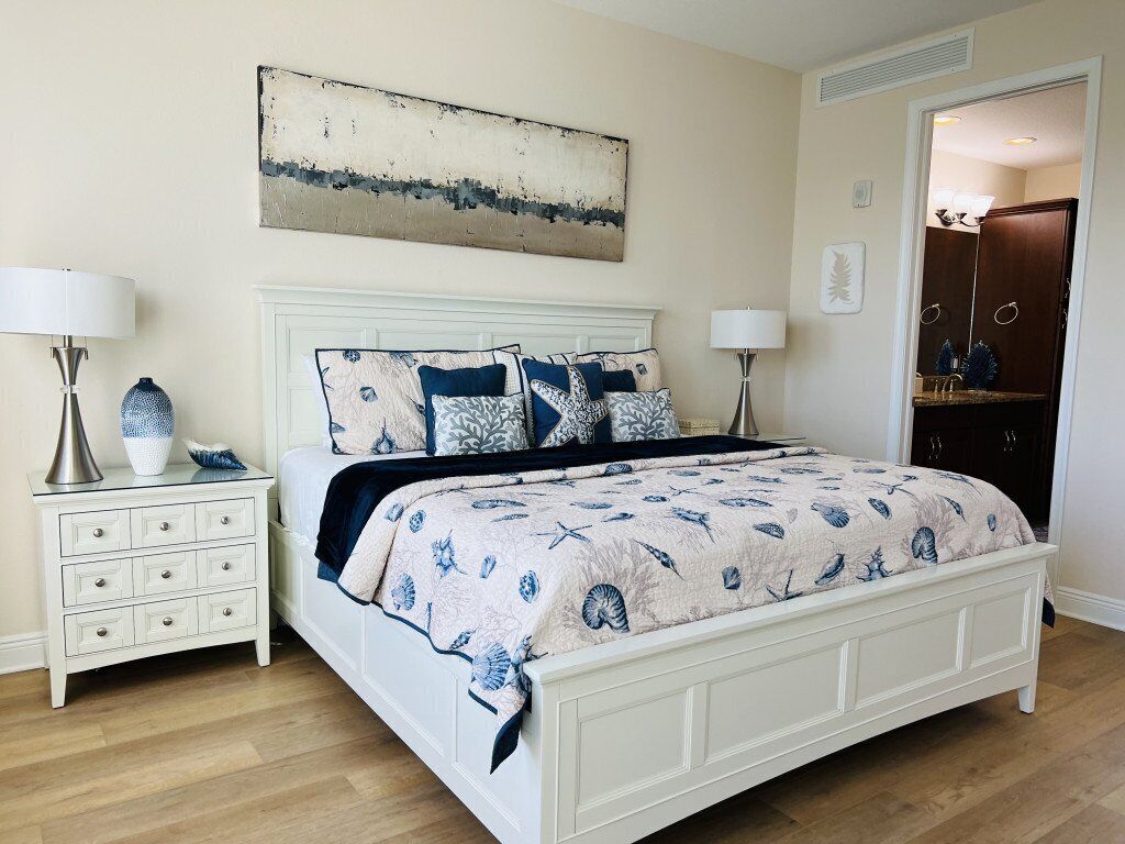 A bedroom with a white bed, matching nightstands, and a large abstract painting on the wall.