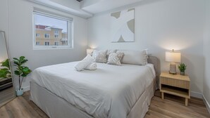 Un dormitorio moderno con una cama grande, una mesita de noche con lámpara, una ventana y una planta.