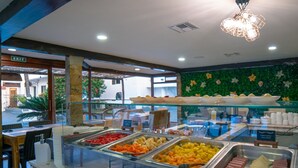 Een buffet met diverse gerechten, een glazen vitrine en een groene wand met bloemversiering.