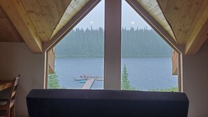 Une pièce dotée d’un plafond en pente et d’une grande fenêtre donnant sur un lac et une forêt.