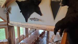 Un coin repas avec une longue table en bois et des chaises, une tête d’ours empaillée accrochée au mur et une enseigne indiquant le Crystal Lake Resort.