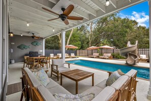 Un espacio exterior techado con piscina, asientos y una parrilla.