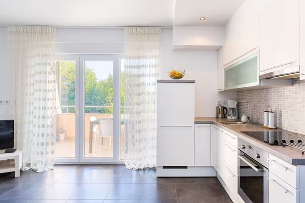 A modern kitchen with white cabinetry, a built-in oven, and a dining area with a table and chairs.