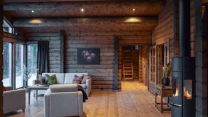 L’intérieur d’une cabane en rondins, avec une cheminée, un canapé, une table basse et une vue sur l’extérieur.
