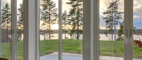 A room with a large sliding glass door leading to a patio with a view of trees and a body of water.