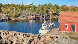 En hamn med en röd byggnad, en vit båt som heter ”Garten Handelop” och en stenig strand.