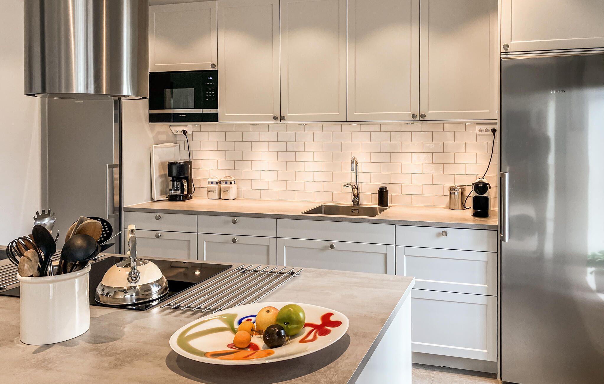 A modern kitchen with white cabinets, stainless steel appliances, and a variety of utensils.