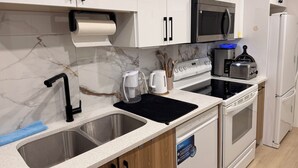 A modern kitchen with white cabinets, a stainless steel sink, a black countertop, a microwave, a toaster, and a dishwasher. - 2-Bed, 2-Bath Home: Perfect for Work, Relaxation, and Exploring Calgary & Banff. (Calgary)