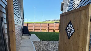 A narrow pathway leading to a wooden gate with a decorative window, flanked by wooden siding and a concrete path. - 2-Bed, 2-Bath Home: Perfect for Work, Relaxation, and Exploring Calgary & Banff. (Calgary)