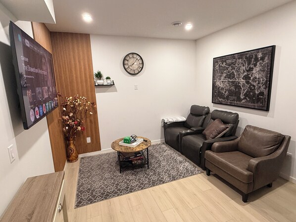 Una sala de estar moderna con un sofá, una mesa de centro, un reloj y un televisor montado en la pared.