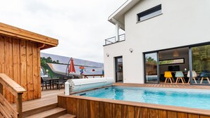 Un área de piscina exterior moderna con un deck de madera, un jacuzzi y un tobogán.