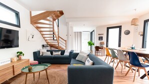 Una sala de estar moderna con una escalera, un conjunto de sofás, un comedor y un televisor montado en la pared.