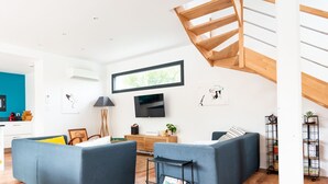 Una sala de estar moderna con una escalera, un televisor de pantalla plana y techo de madera.