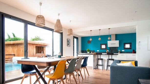 Una cocina moderna con paredes azul verdoso, un comedor de madera y vistas a una piscina exterior.