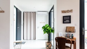 Un interior moderno con una puerta blanca, una planta en una cesta de mimbre, una silla de madera y un cartel que dice 'WELCOME'.