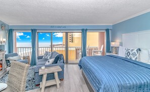 A room with a bed, a sofa, a small table, and a view of the beach.