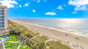 Ein Strand mit einem Hotel im Hintergrund, einem klaren Himmel und ruhiger See.