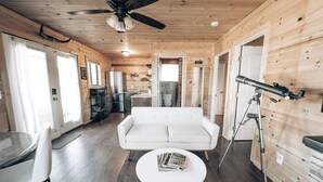 A cozy cabin interior with a white sofa, a dining table, and a telescope.
