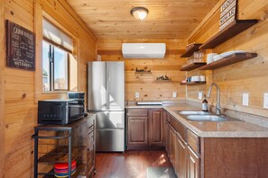 A cabin-style kitchen with wooden walls, a refrigerator, a microwave, a sink, and a window. - Cozy Cub Cabin, Wilderness Retreat Williams AZ near Grand Canyon, Fire pit (Williams)