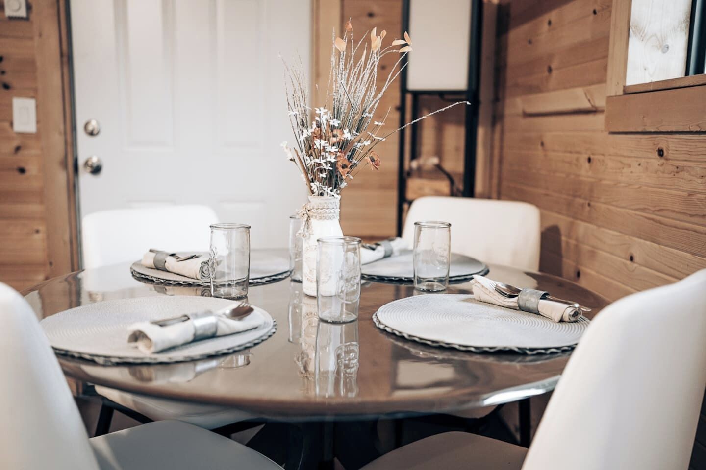 A dining table set with placemats, glassware, and a centerpiece of dried flowers.