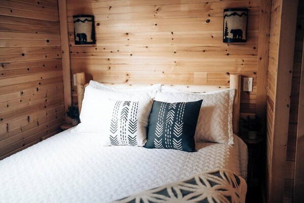 Habitación de cabaña de madera con una cama, dos almohadas y dos luces fijadas a la pared.
