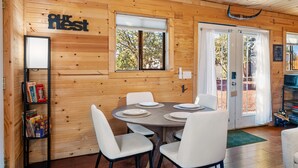 A wooden cabin interior with a dining table, chairs, a bookshelf, and a sign reading 'Our Best.'